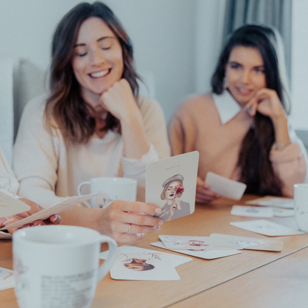 Zwei Freundinnen an einem Tisch, zwischen ihnen Karten und eine Tasse