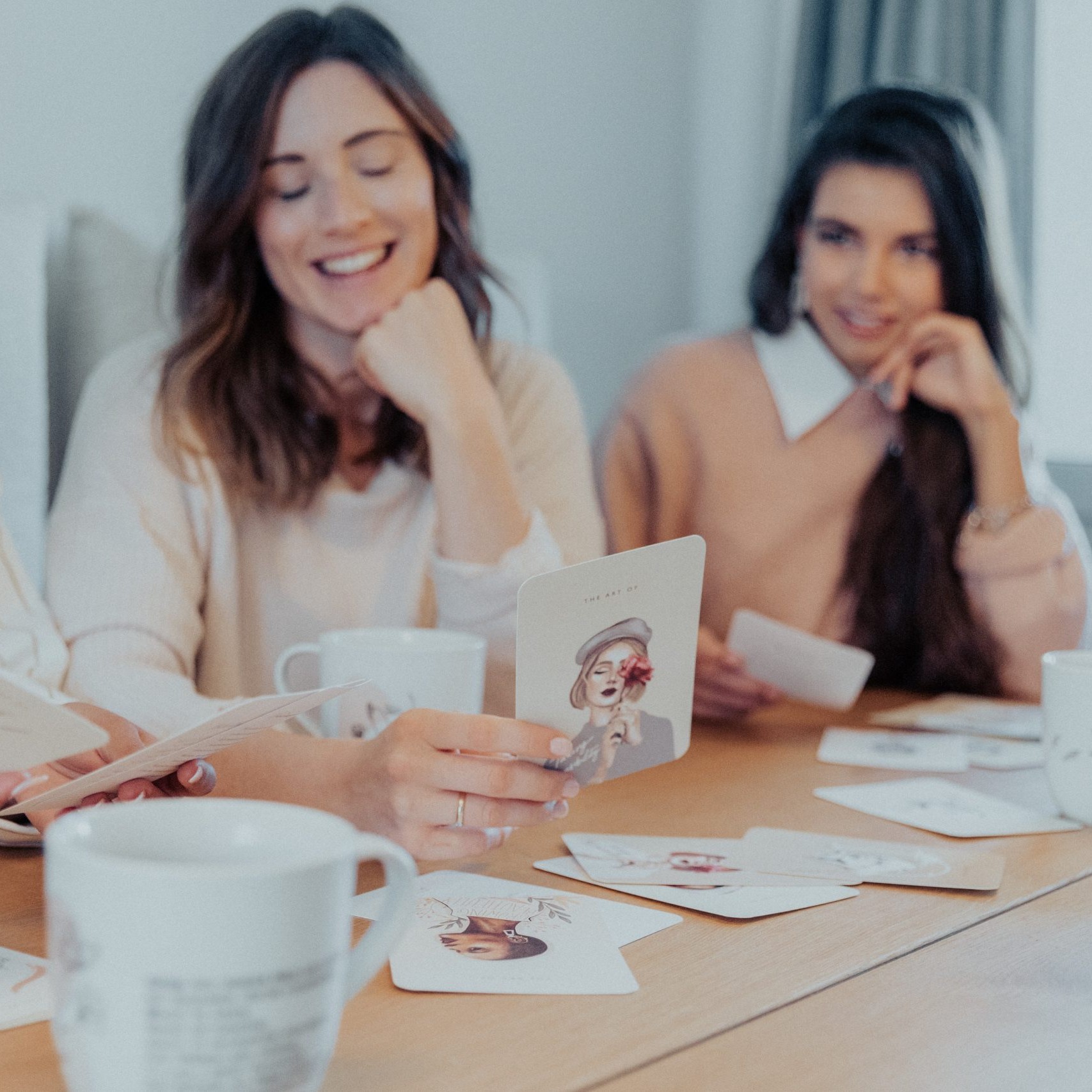 Zwei Freundinnen an einem Tisch, zwischen ihnen Karten und eine Tasse