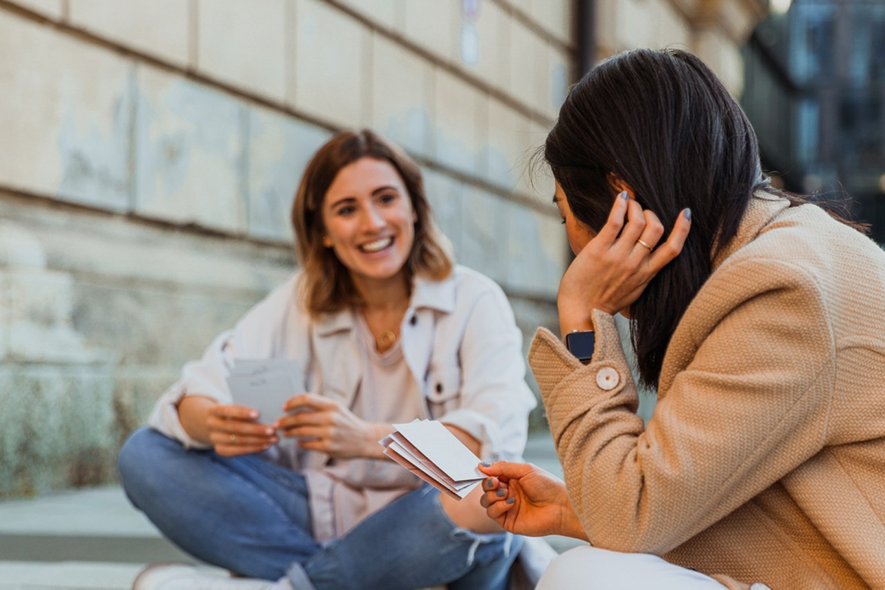 Zwei Freundinnen sitzen auf dem Boden und reichen sich Affirmationskarten