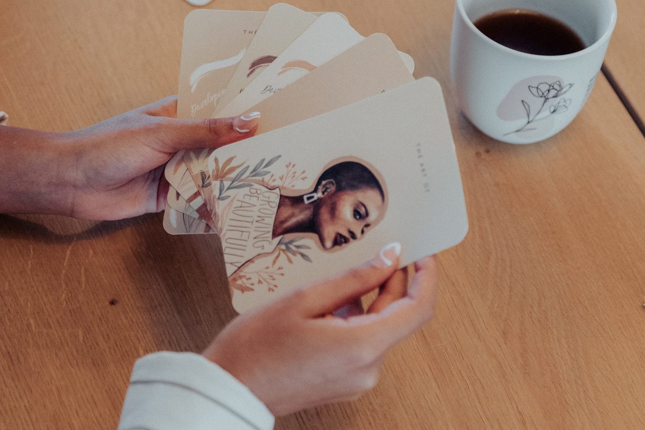 Zwei Hände fächern Karten des Reflexionskarten-Sets auf, daneben eine Tasse Kaffee