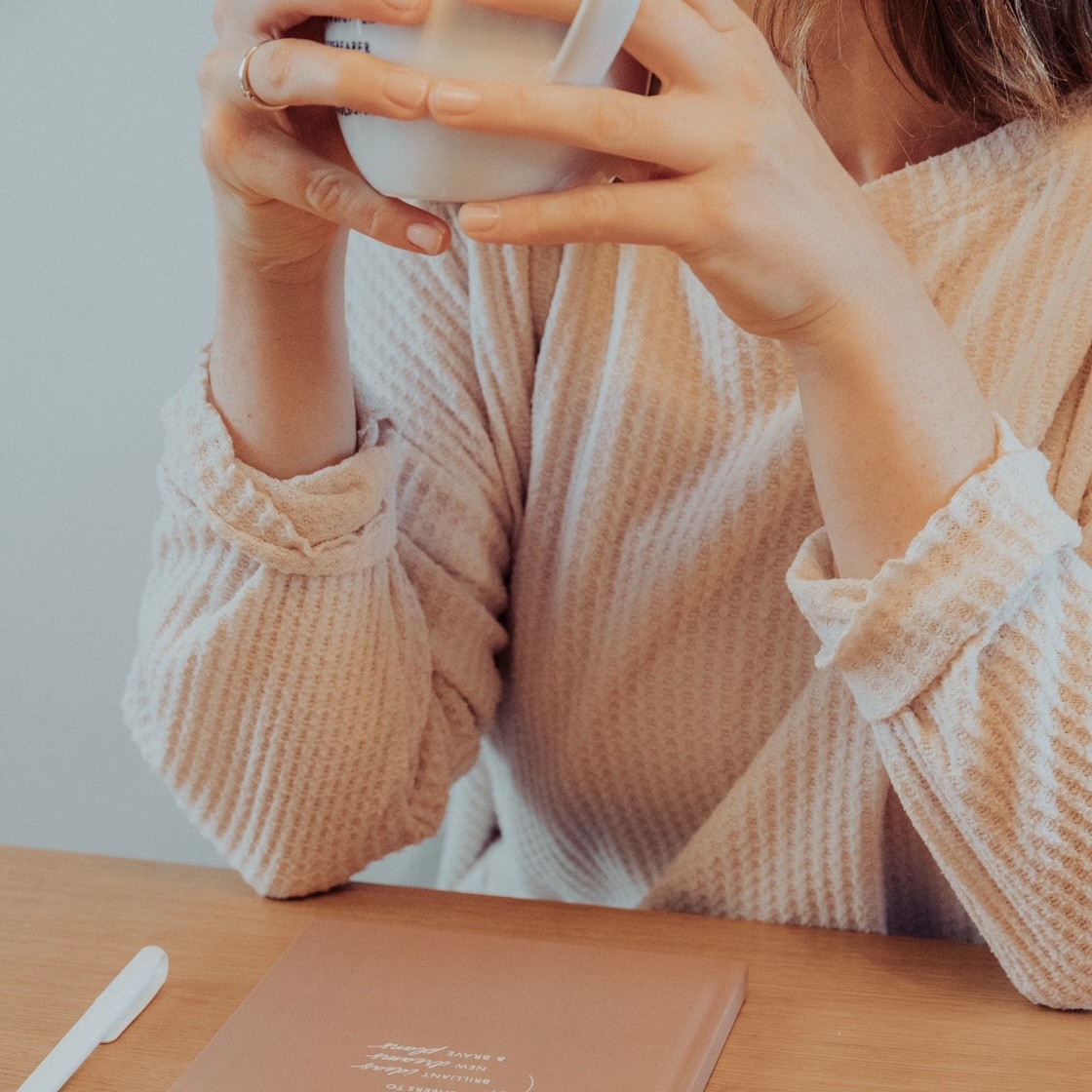 Frau trinkt Kaffee am Schreibtisch, daneben ein Notizbuch
